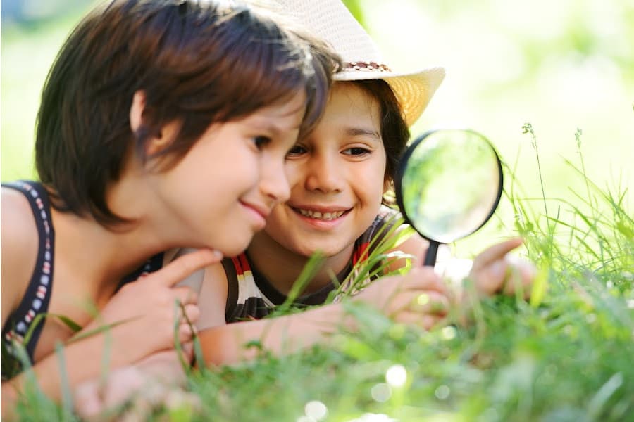 two children outside looking at a grass through a magnifying glass